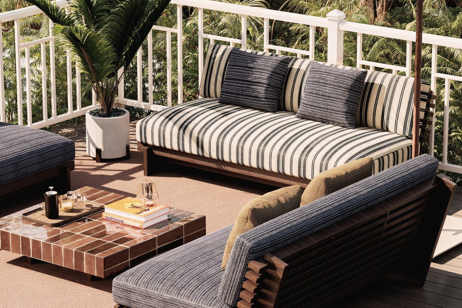 Salon d'extérieur sur une terrasse tropicale avec un canapé en bois garni de coussins à rayures bleu marine et blanc, un fauteuil à lattes en bois sombre avec coussins kaki, et une table basse en carrelage terre cuite avec livres et bougie, entouré de végétation luxuriante.